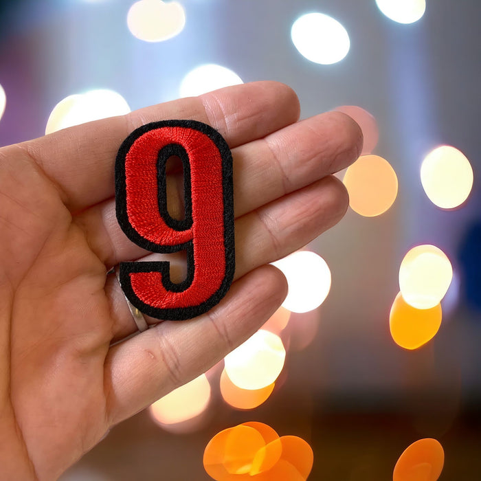 5cm red embroidered iron-on patch number 9 with a contrasting black felt border, held in a hand
